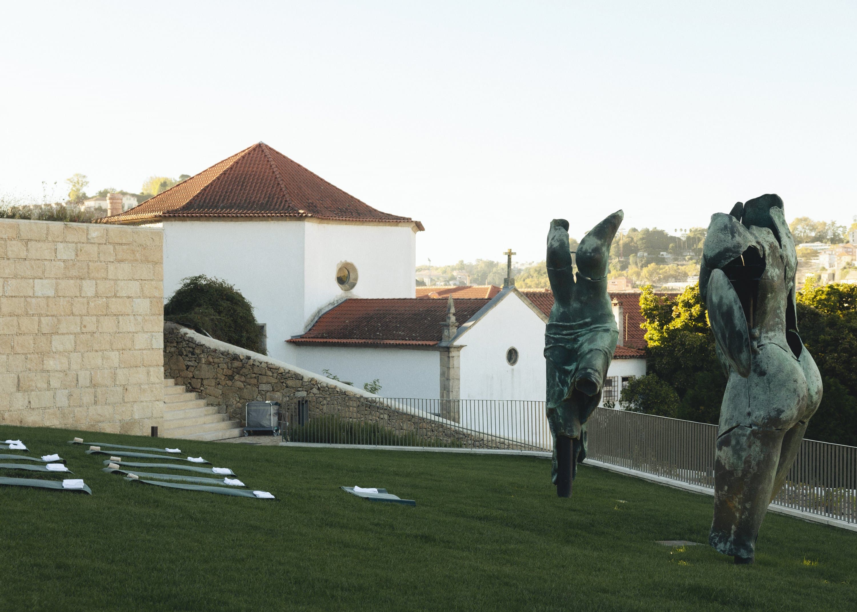 Yoga mats laid out on a lawn among bronze sculptures, above the river.